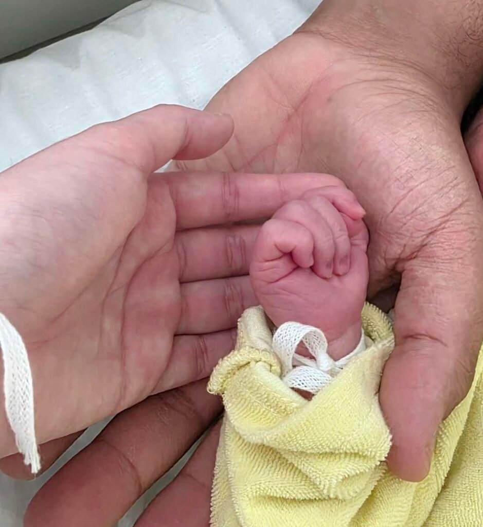 Erste Momente nach der Geburt: Die Hand des Neugeborenen gehalten von Mama und Papa