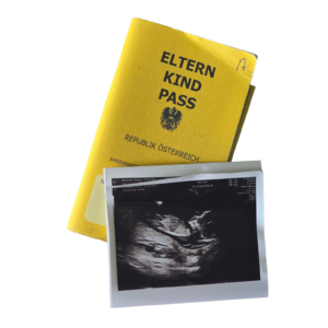 Ein gelber österreichischer Eltern-Kind-Pass, auf dem ein schwarz-weißes Ultraschallbild vom ersten Frauenarzt-Termin liegt.